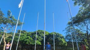 A servidora Santinha Girardi, o reitor Eustáquio de Castro e a vice-reitora Sonia Lopes posam em frente aos mastros das bandeiras. 