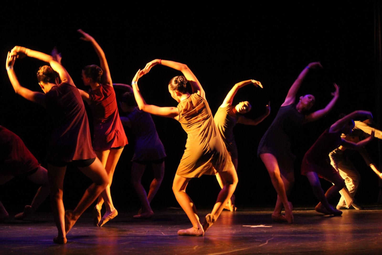 Grupo de bailarinas, vestidas cada uma de uma cor, fazem apresentação de dança contemporânea em um palco