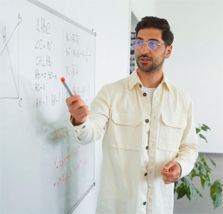 Imagem de um professor jovem em sala de aula, escrevendo no quadro branco